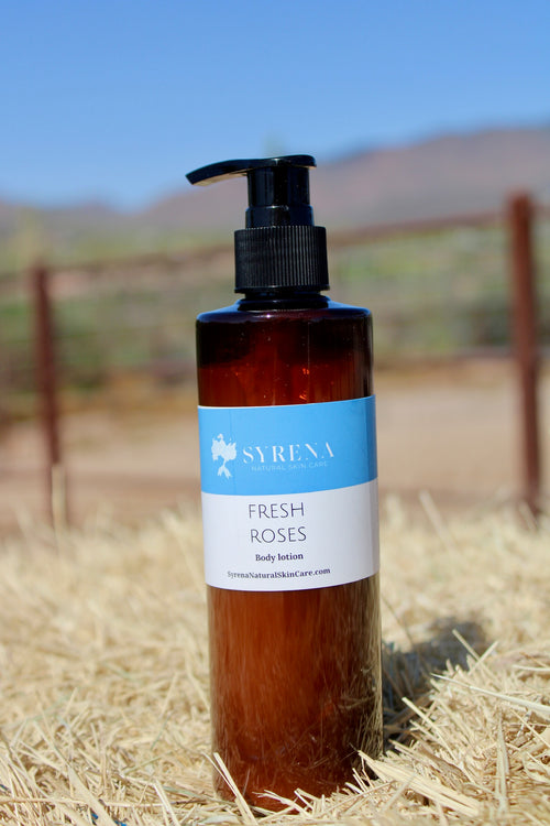 Brown bottle of Syrena Fresh Roses body lotion on hay with a blurred outdoor background